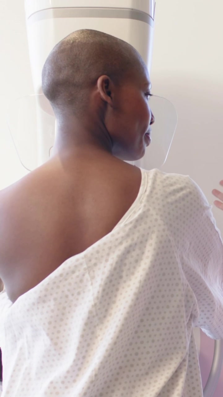 Video verticale: Paziente si gira, sistema il camice e si allunga verso lo scanner in clinica, preparandosi per la scansione.