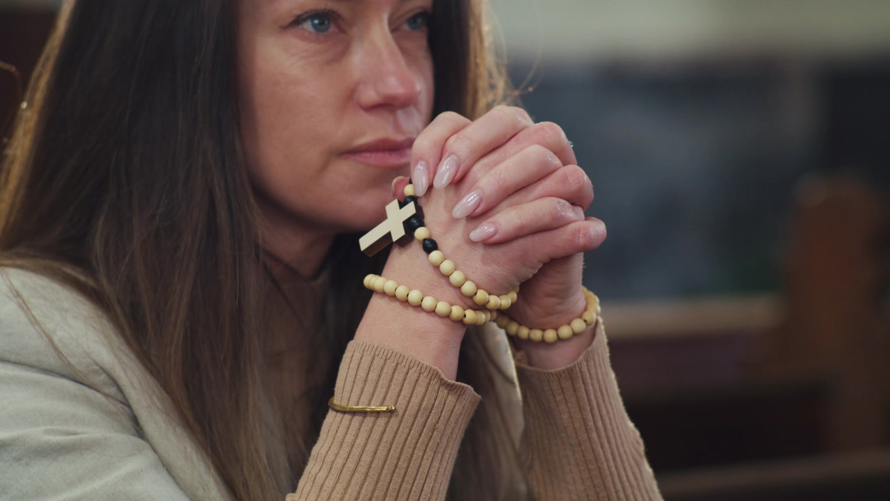 Donna con le mani giunte in preghiera che tiene un rosario cattolico con una croce pendente, concetto di fede