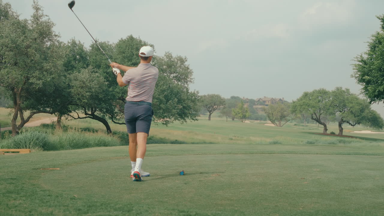 A male golfer hits a powerful driver off the tee box and watches the ball flight in slow motion. The clip captures focus, technique, and the fluid motion of a confident swing on the course.