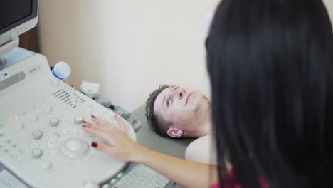 Closeup-view-of-young-female-doctor-with-long-hair-in-rose-uniform-is-screaning-her-patient's-heart-with-ultrasonography,-looking-at-the-screen,-and-consulting.