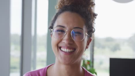 Portrait-of-smiling-biracial-creative-businesswoman-wearing-glasses-in-modern-office-interior