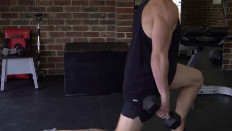 muscly man in home gym exercising shot from side walking lunges with dumbbells