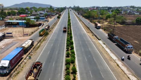 Aerial-dolly-shot-of-large-trucks-traveling-along-a-highway-in-Maharashtra,-India