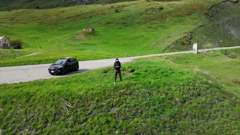 Rising-aerial-of-drone-pilot-and-car-in-summer-alpine-mountain-landscape,-France