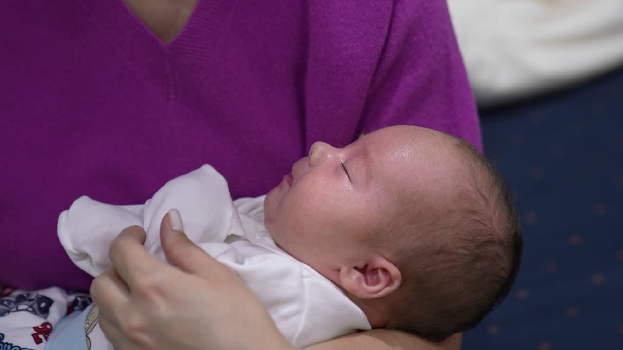 Sweet kid sleeping and then waking up slowly and waving his hands. Infant in mom's hands yawning sweetly. Close up.