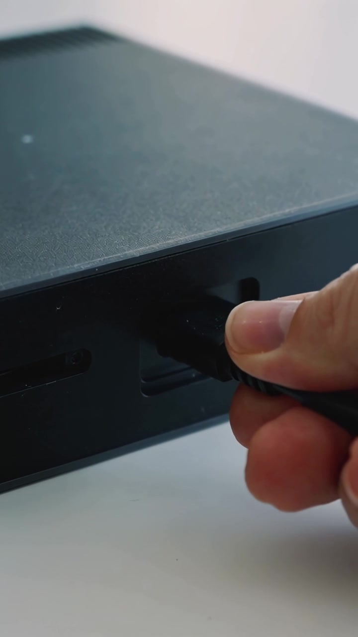 Vertikal video: Højre hånd kommer ind, justerer og indsætter USB-stik i sort boks på skrivebord, forbinder.