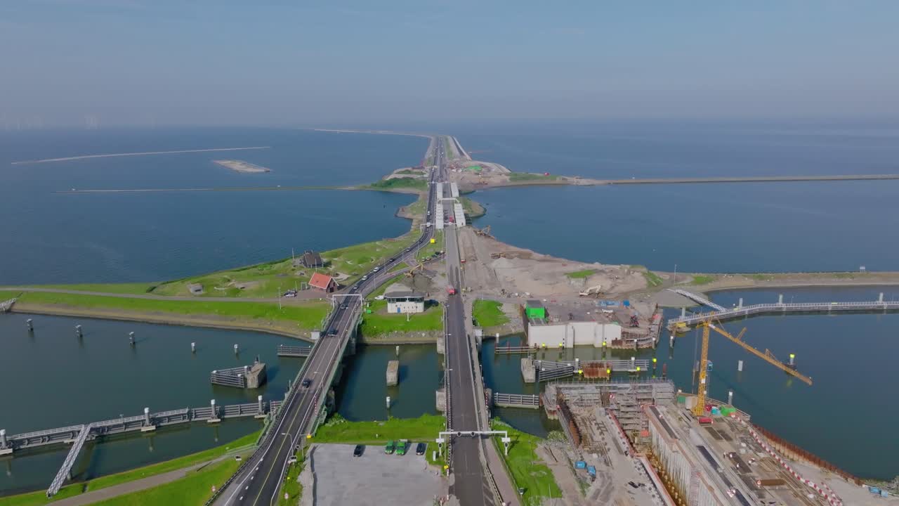 Aerial zoom out showing the Afsluitdijk dam and locks system stretching across the sea under clear blue sky