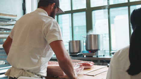 bearded butcher laying down a large cut of meat to prepare