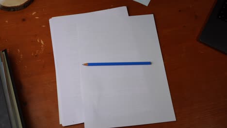 un crayon bleu est placé sur un morceau de papier sur un bureau en bois par une jeune main droite, puis le saisit à nouveau et l'emporte