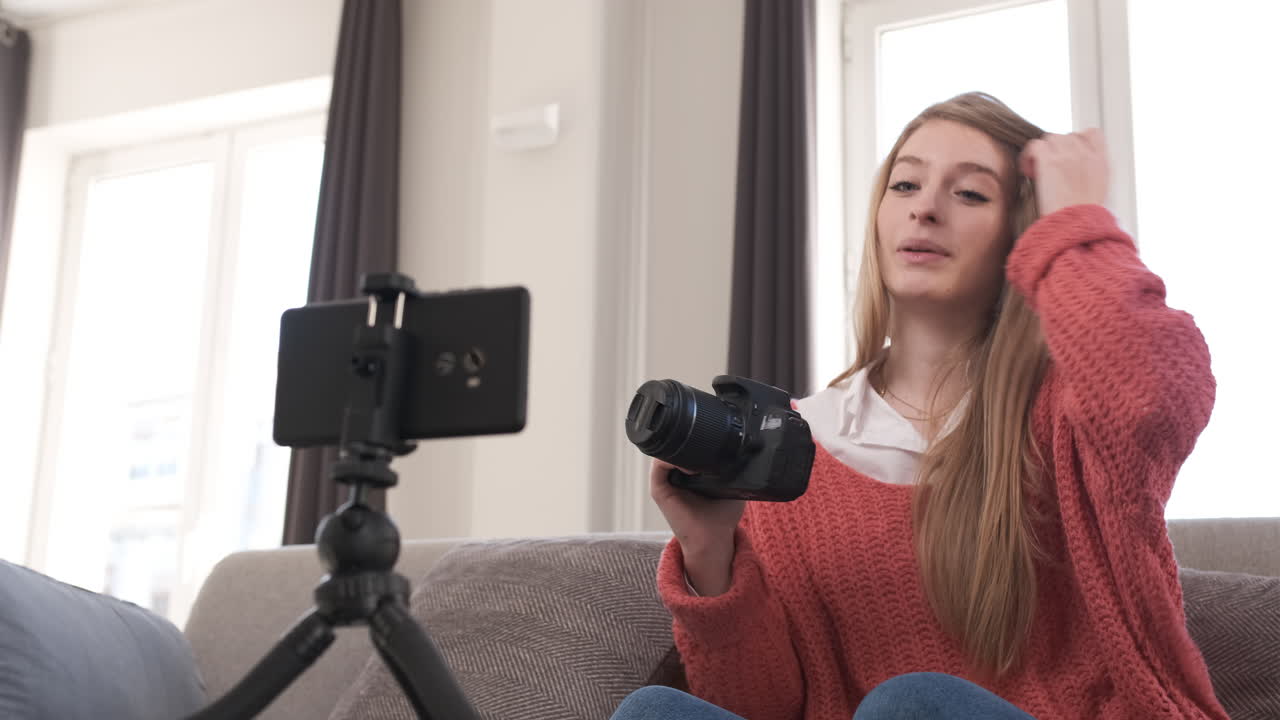 Young woman talking on mobile camera, explaining a photo camera. Content creator concept