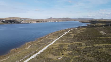 wind sweeps across the falkland islands' coast, revealing a distant town against a backdrop of ocean and sky