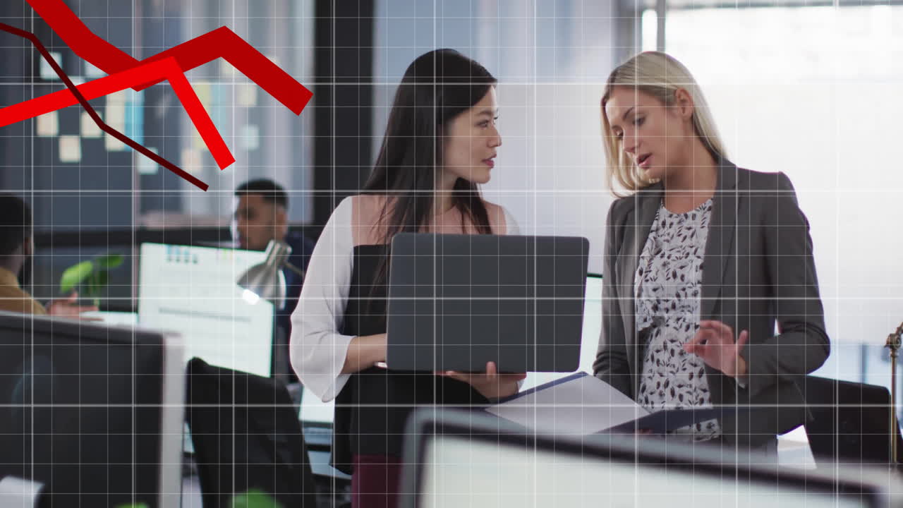Dwie kobiety omawiające strategię biznesową z laptopem na tle animacji spadającego wykresu finansowego.