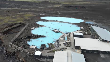 disfruta de la tranquilidad aérea sobre los baños naturales de mývatn, donde las piscinas calientes de color azul profundo ofrecen un sereno contraste con la extensión del lago mývatn en vívidos 4k