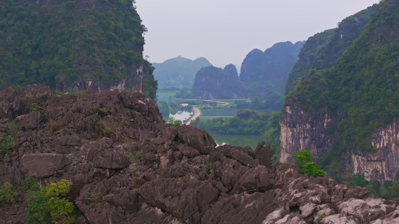 el impresionante paisaje de ninh binh, vietnam, con altos acantilados de piedra caliza, un sendero sinuoso y una exuberante vegetación con cuerpos de agua reflectantes