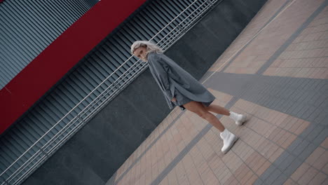 chica modelo posando cámara cerca de un edificio urbano moderno en el centro de la ciudad.