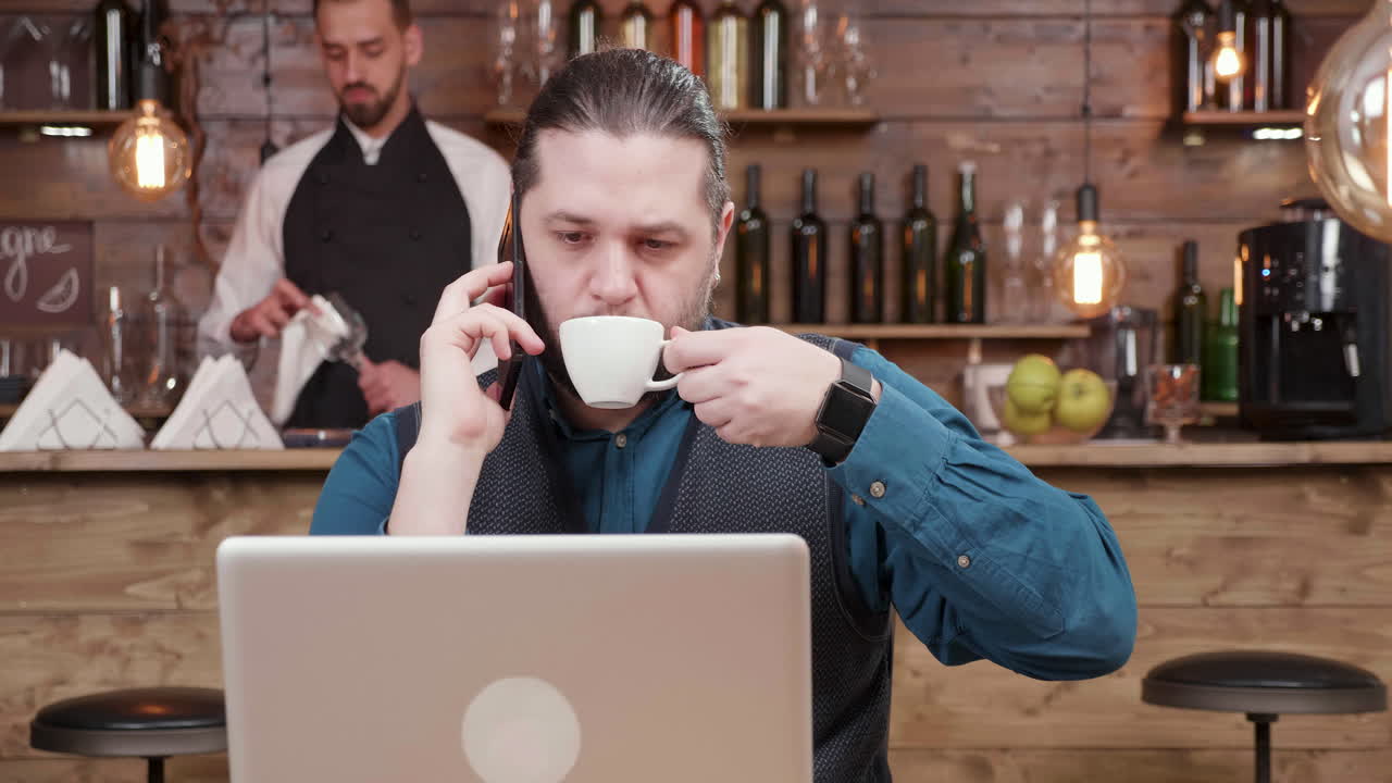 Uomo che usa un laptop e parla al telefono in un bar