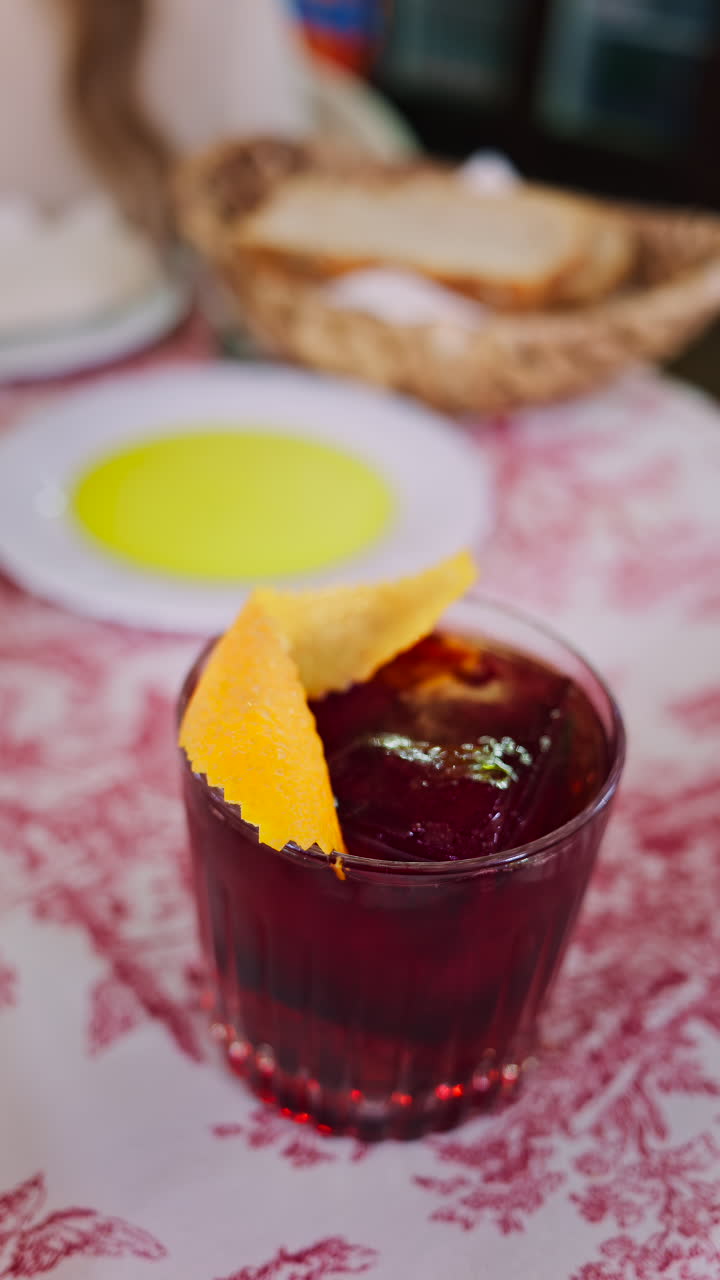 Close up of a negroni cocktail on a red and white tablecloth at a restaurant. Vertical