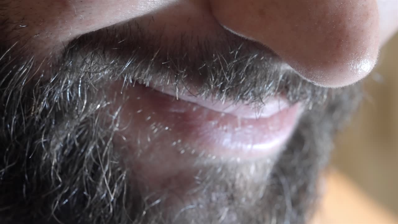 A slow-motion close-up of a man's beard around his mouth as he smiles, capturing the movement and details.