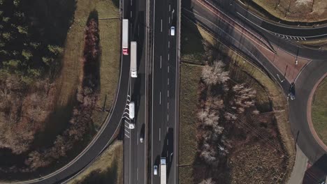 an aerial video of a multi-lane highway with cars and trucks in motion. the surrounding landscape features green grass, trees, and intersecting roads, creating a dynamic urban-rural contrast.