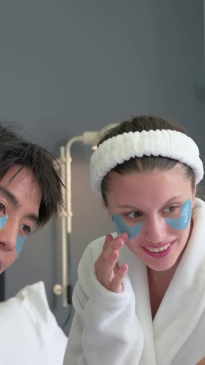 Vertical video: Shifting man at home, couple in robes joining and checking blue patches with mirror