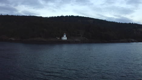 moody lighthouse drone. drone flying toward lighthouse (wide shot) over water at sunset in the pacific north west san juan islands. birds flying over ocean with forest in background. lighthouse 4k