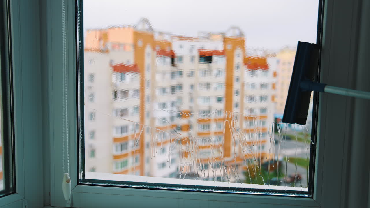 Window cleaning brush making glass clean. House worker washing window with a special brush inside the room on urban background.