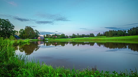 Countryside-lake-with-green-trees-and-cottage-in-summer-sun,-timelapse