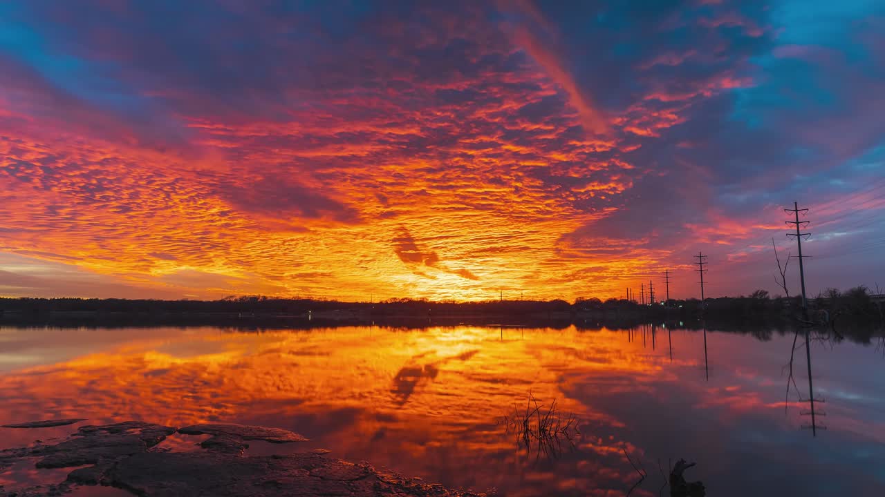 해가 지는 것에서 불타는 하늘은 빨간색에서 파란색으로 진정됩니다. 어두운 빛이 후퇴함에 따라 아래의 물에 반사됩니다.