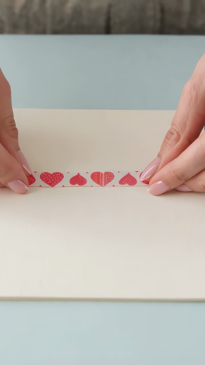 Vertical video: Holding strip taut, woman's hands smoothing heart tape on desk, forming even border