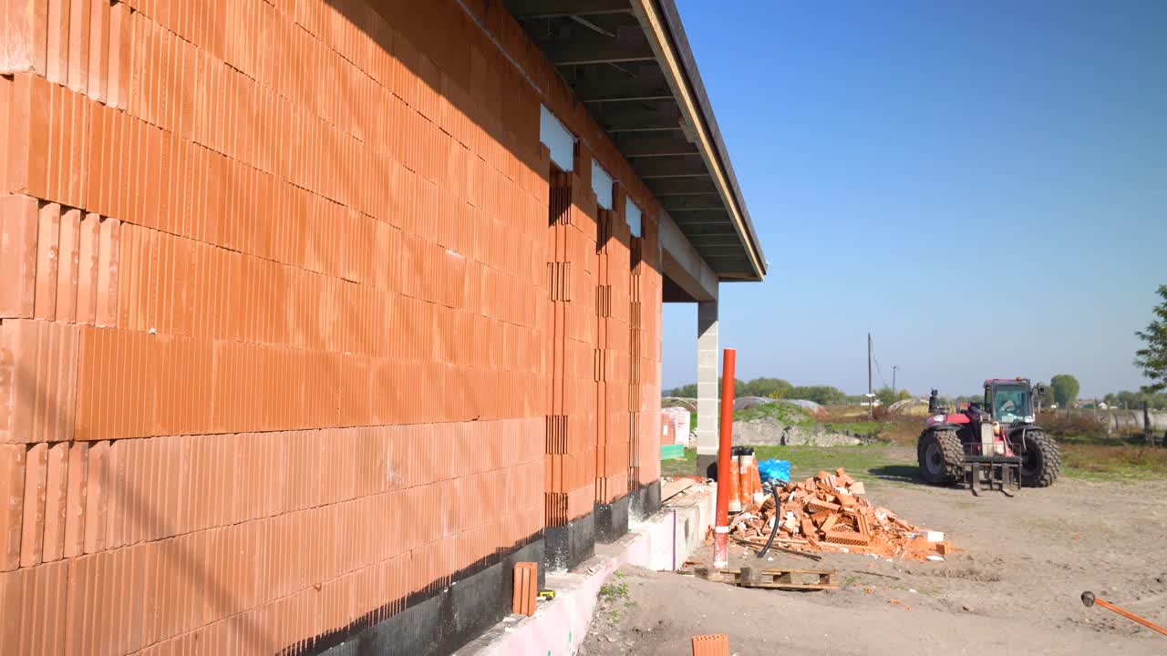Brick wall of unfinished house with construction site and tractor in background