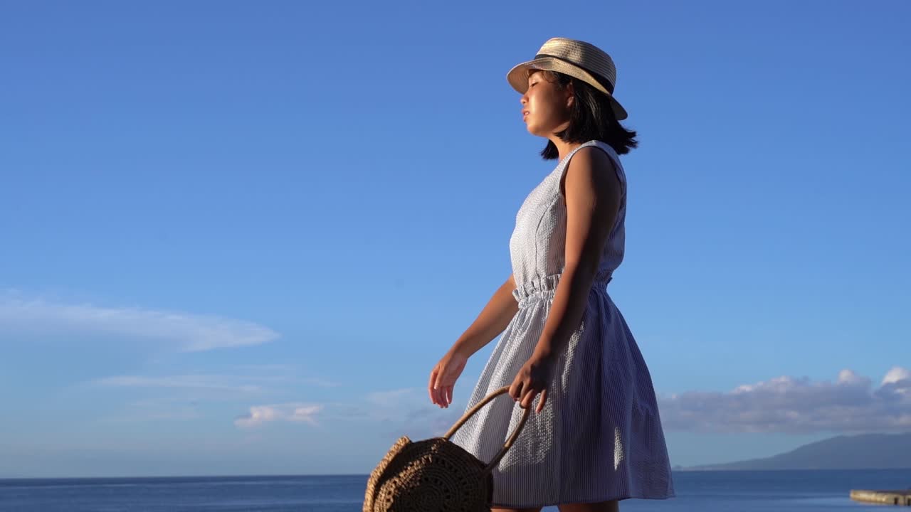 아름 다운 맑은 날에 바다 앞에서 가방을 들고 여름 드레스에 일본 소녀-옆으로 추적 샷 슬로우 모션