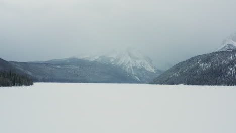 Low-aerial-over-beautiful-frozen-lake-with-large-foggy-mountains-behind