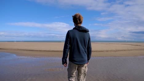 slow motion shot of a man walking across a beach at low tide near the sete salt flats