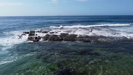 toma aérea de paisaje de drones de un niño surfista caminando sobre rocas arrecife costa central olas océano pacífico nsw australia 4k
