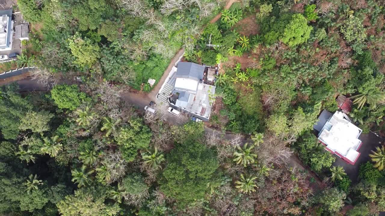 Aerial drone view of a traditional Kerala village home in India surrounded by lush tropical greenery, coconut trees, and countryside roads, showcasing serene rural lifestyle and natural beauty