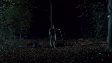 woman digging a shallow grave next to a dead body in a spooky forest at night