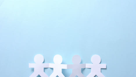 close up of people holding hands made of white paper on blue background with copy space