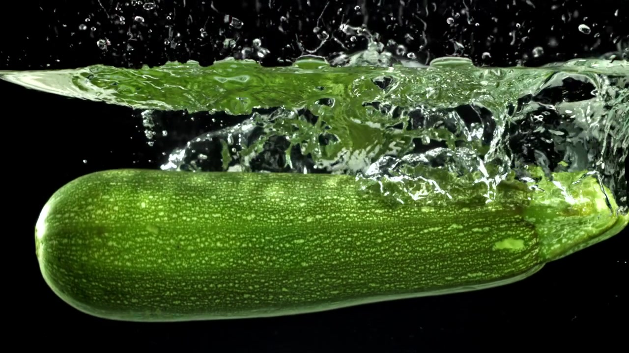 Zucchine verdi fresche che si tuffano nell'acqua limpida al rallentatore.