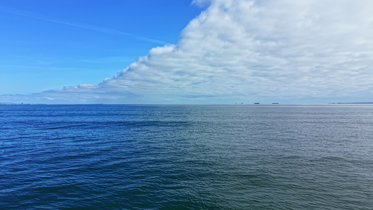 Ampia vista sull'oceano che mostra nuvole e navi lontane in una giornata limpida con cielo blu sullo sfondo.
