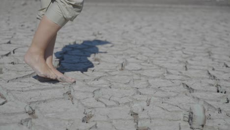 pies descalzos caminando lentamente sobre tierra seca y agrietada, durante una sequía.