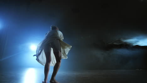 modern dance woman in a white dress dances a modern ballet jumps on the stage with smoke in the blue spotlights.