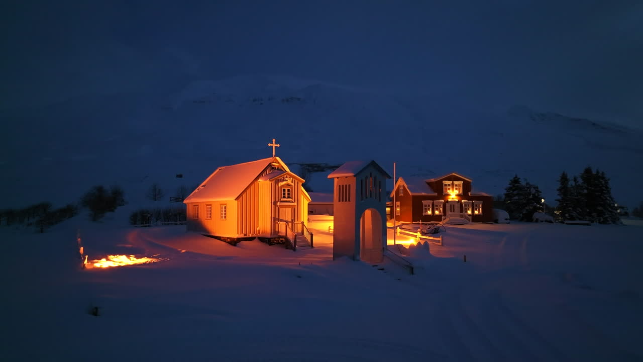 iglesia iluminada en naranja junto a un hotel en una espesa capa de nieve en islandia por la noche