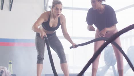 video de una entrenadora de fitness femenina diversa alentando a una mujer que lucha contra las cuerdas trabajando en un gimnasio