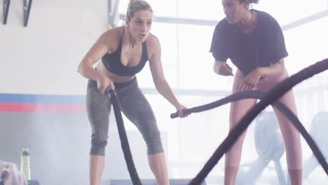 video of diverse female fitness trainer encouraging woman battling ropes working out at a gym