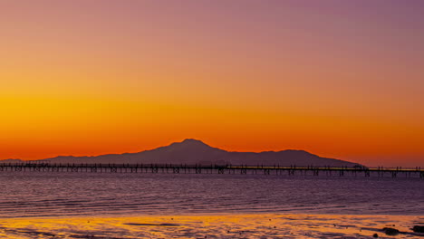 Sun-setting-down-casting-glow-on-sky-above-mountain-silhouette,-time-lapse