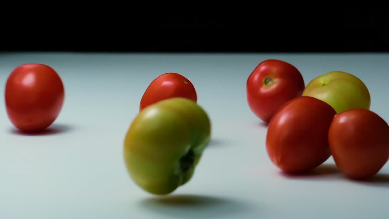 los tomates rojos, verdes y amarillos caen y ruedan sobre la mesa, cámara lenta