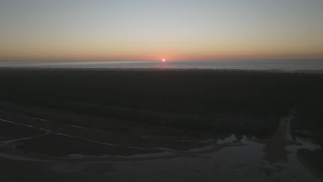 sun setting over sand dunes of dunes city, oregon, car drives along sand through trees towards ocean, aerial pullout.