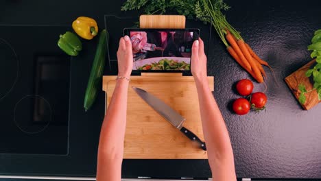 tiro de ojo de pájaro de una mujer que puso una tableta en una tabla de cortar con una receta en una tableta en una cocina moderna y hierbas y verduras frescas