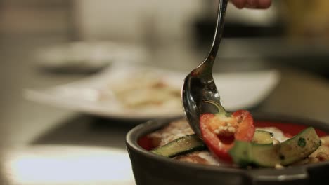 Chef-putting-grilled-Courgette-slices-on-grilled-vegetables-with-fried-egg-and-more-vegetables-on-a-side-dish-behind