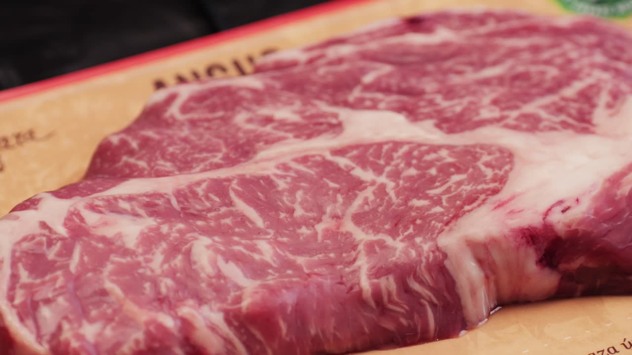 胡椒、塩、ローズマリーが添えられた新鮮な霜降り牛肉のクローズアップマクロ映像。グリルでジューシーなステーキを調理する準備。プレミアムなオーガニック生和牛肉。高品質4K映像。